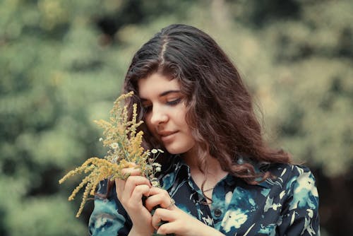 Young Woman in a Floral Shirt Standing Outside and Holding a Bunch of Wildflowers