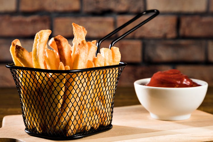 Closeup Of A Frying Basket With French Fries And Bowl Of Ketchup Against Brick Wall