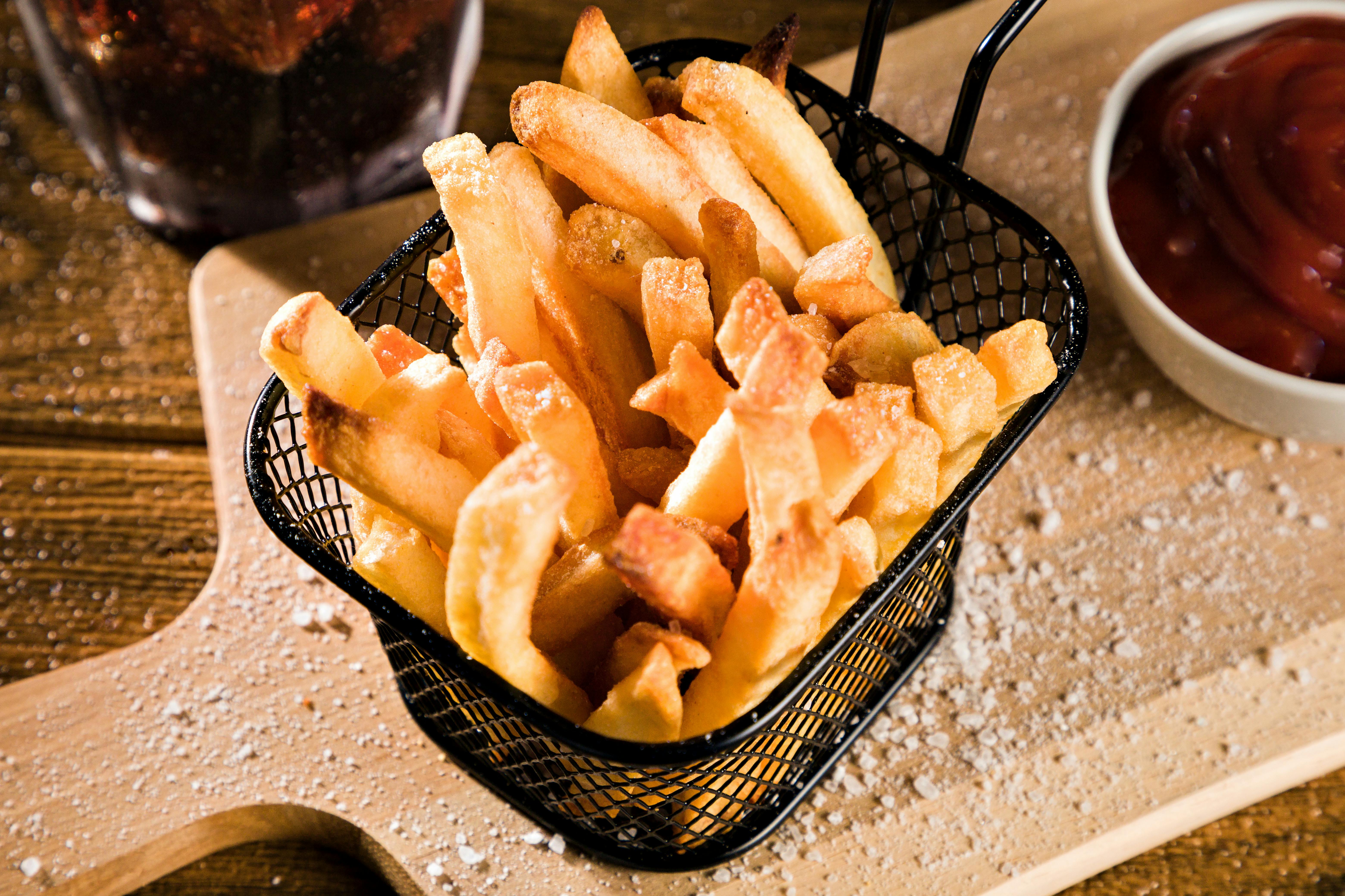 Close-up of crispy homemade French fries served with ketchup on a wooden board. Perfect comfort food.