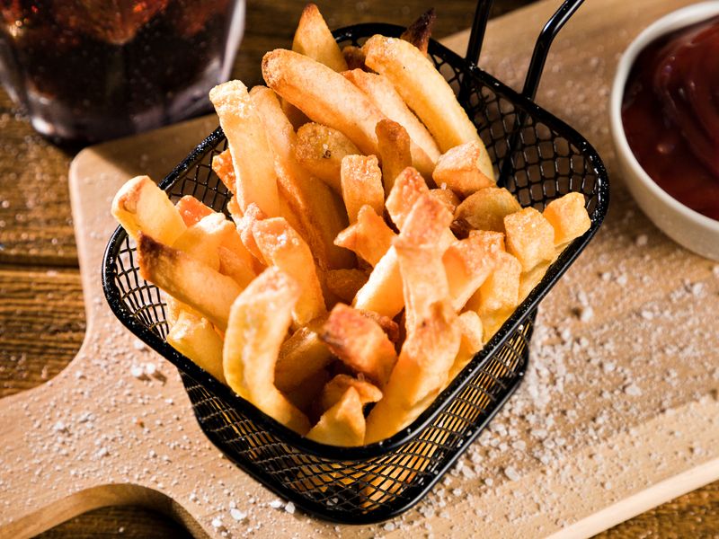 Close-up of crispy homemade French fries served with ketchup on a wooden board. Perfect co