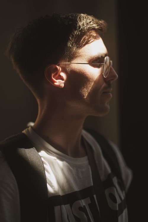 Free Side view portrait of a man in glasses with soft lighting creating a moody atmosphere. Stock Photo