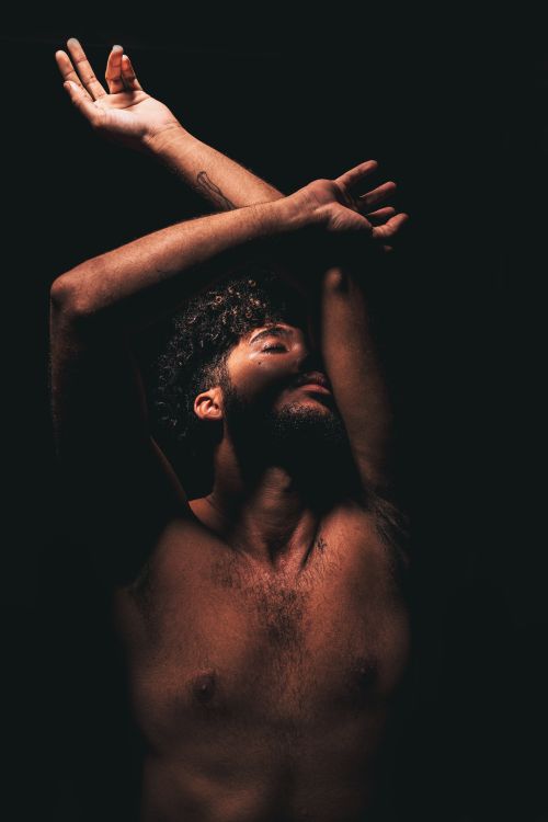 Free Artistic portrait of a bearded man with raised arms, captured in a moody studio setting. Stock Photo