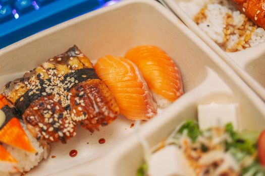 Close-up of sushi nigiri assortment featuring salmon and eel with sesame seeds in a takeout container.
