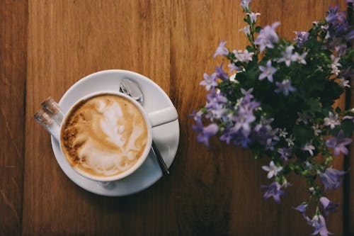 Free A beautifully crafted cappuccino paired with delicate purple flowers on a wooden table. Stock Photo