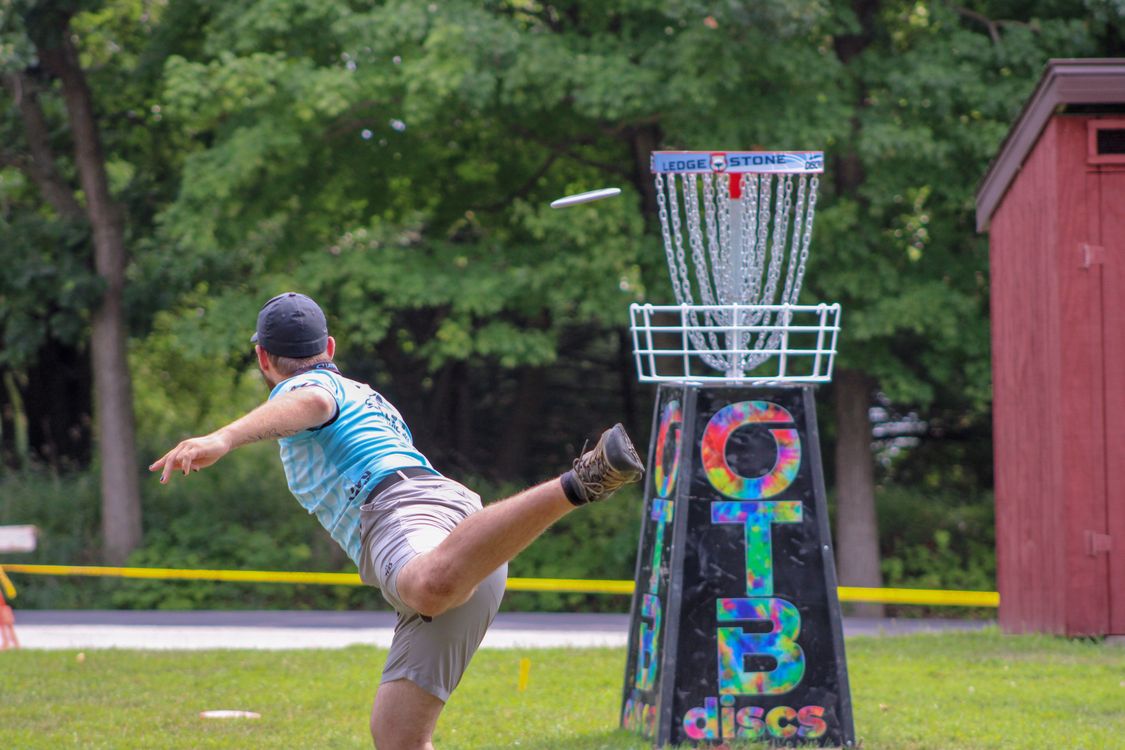 Man playing disc golf, throwing toward a basket on the grass