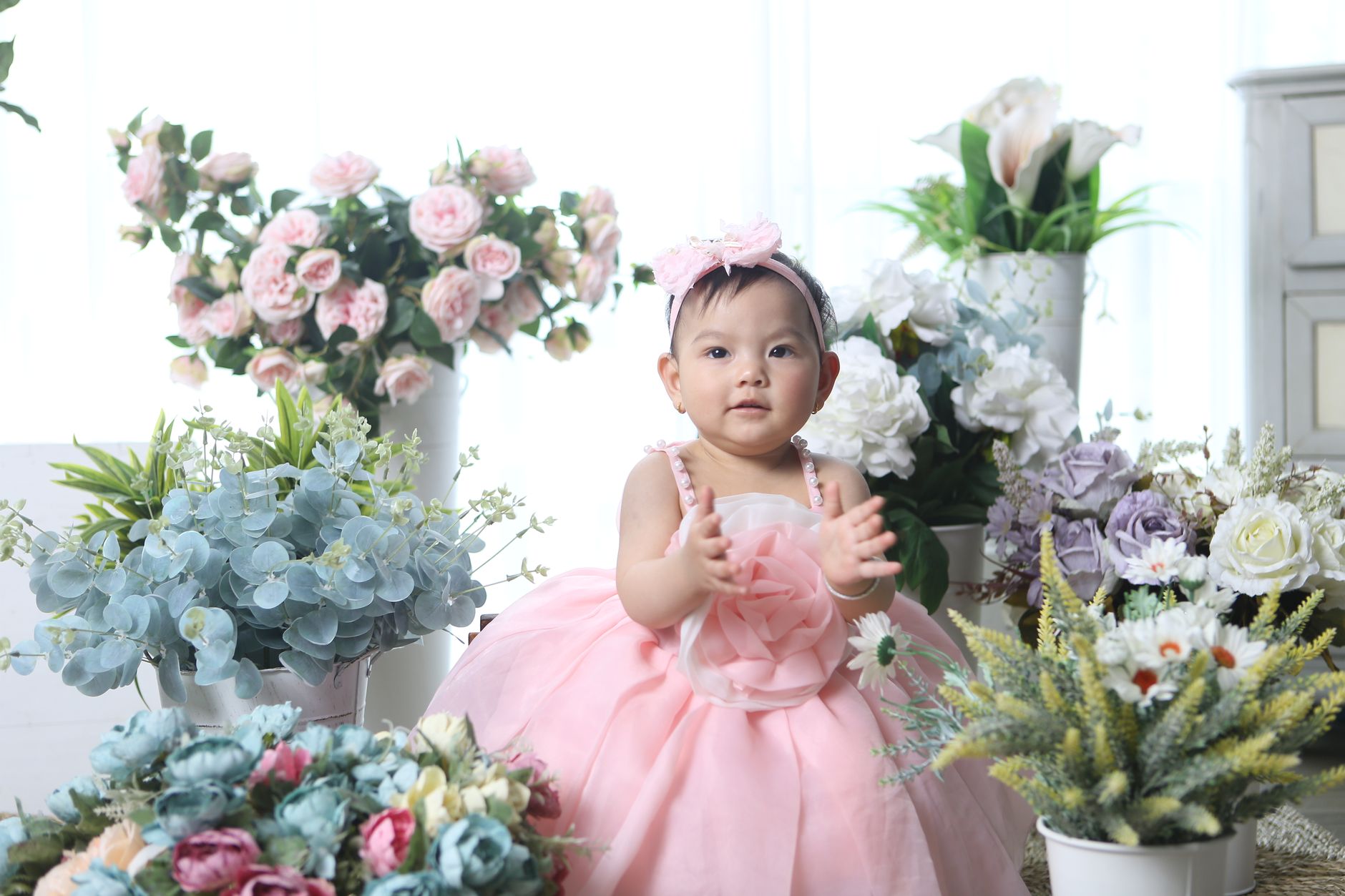 Cute baby surrounded by vibrant floral arrangements, exuding joy and innocence.