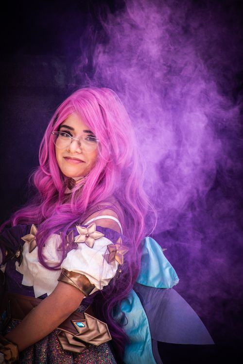 Free A young woman in vibrant cosplay costume surrounded by purple smoke, exuding a fantasy theme. Stock Photo
