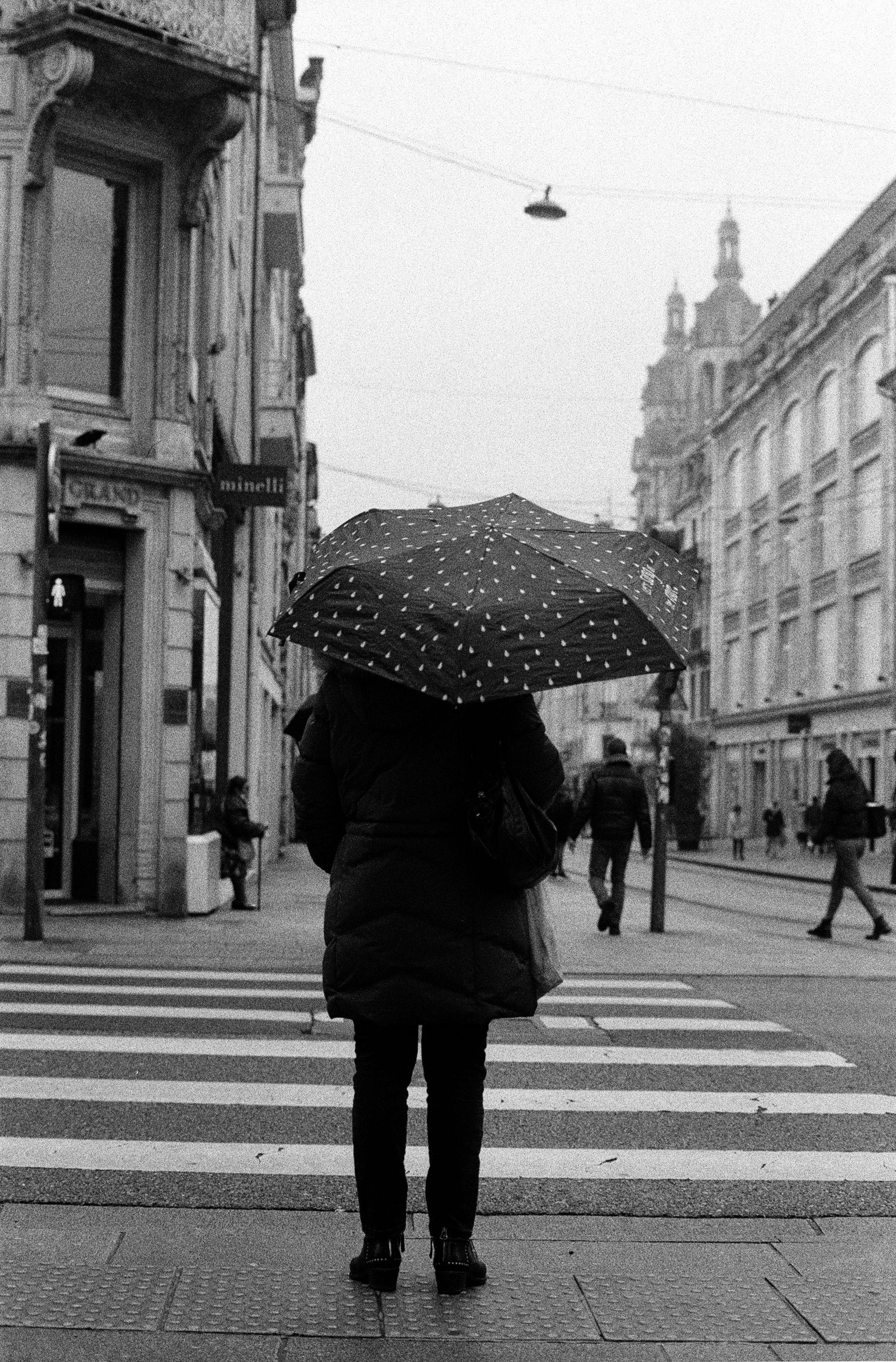 Grayscale Photo of Woman in Black Coat Holding Umbrella Walking on ...
