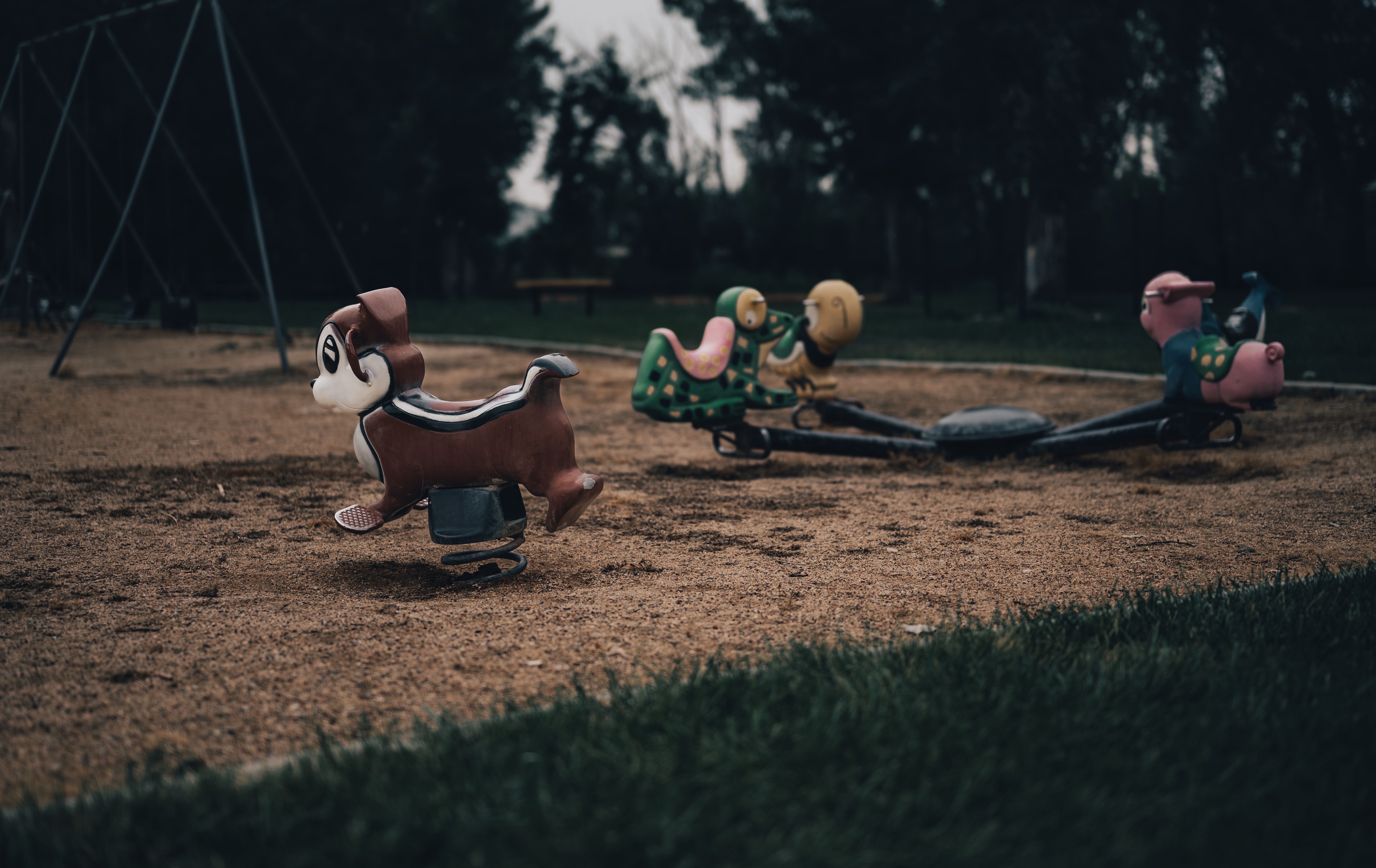 Moody outdoor scene of an empty playground with animal spring rides on a cloudy day.