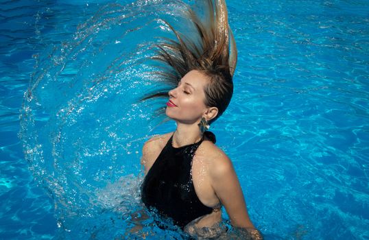 A woman gracefully flips her hair in a sunny swimming pool, embodying summer bliss.