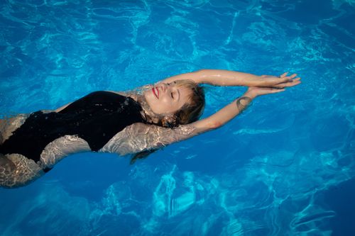 Free A woman enjoys swimming in a pool, floating peacefully with sunlight reflecting off the water. Stock Photo