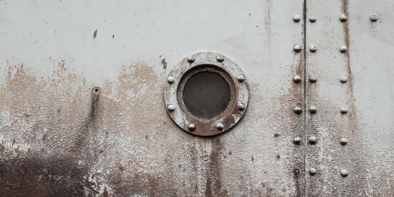 A close-up of a rusty ship porthole on an old weathered steel wall, showcasing a vintage texture.
