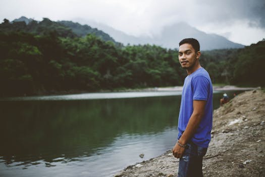 一名年轻人在风景优美、绿树成荫的山间湖泊旁，享受着宁静的时刻
