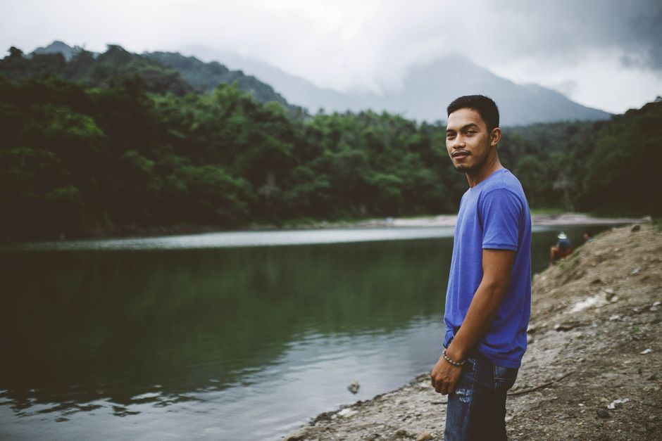 A young man enjoys a peaceful moment by a scenic mountain lake surrounded by lush greenery.