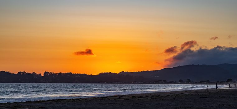 A tranquil beach sunset with silhouettes of people walking along the shore.