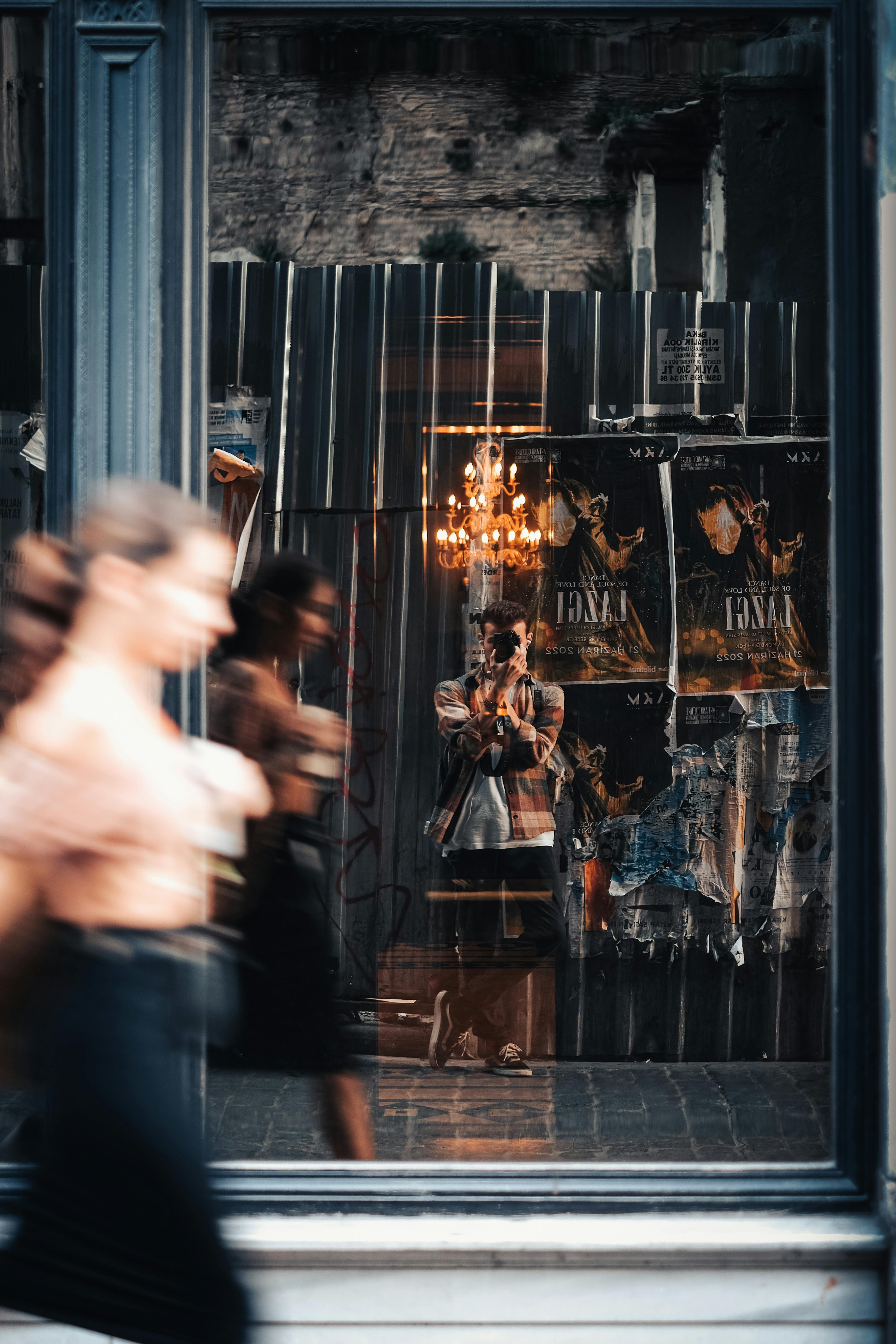 A blurred city street reflected in a window with a photographer capturing the scene.