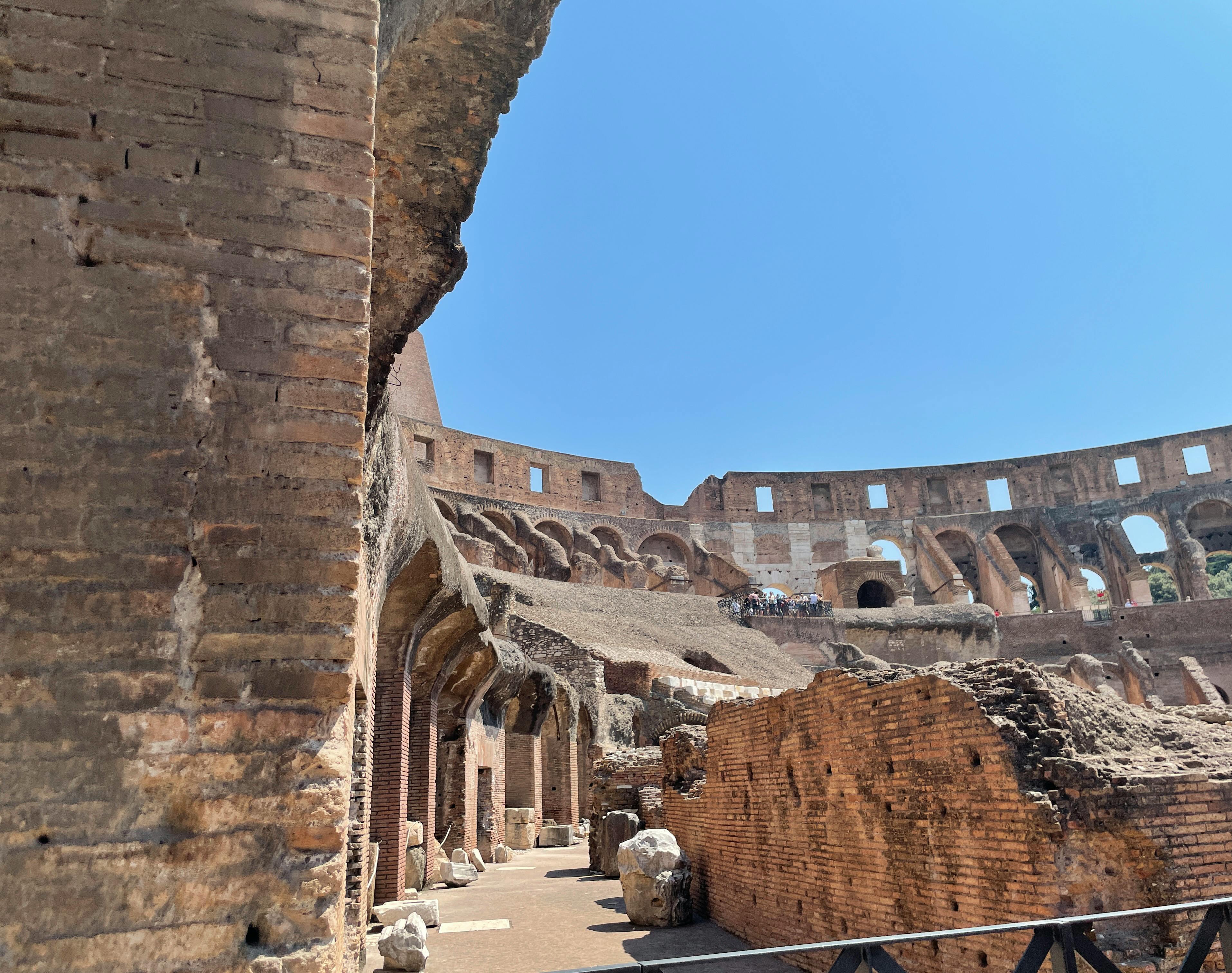 Free Interior view of the ancient Colosseum under a blue sky, highlighting its architectural details. Stock Photo