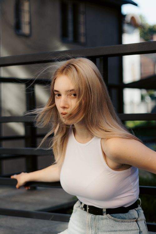 Free Portrait of a blonde woman with long hair posing outdoors against an iron railing. Stock Photo