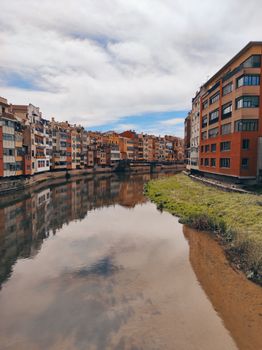 Colorful buildings reflecting in a calm river under a cloudy sky.