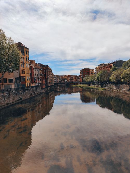 Free Picturesque riverside view with colorful buildings reflected in the calm water under a cloudy sky. Stock Photo