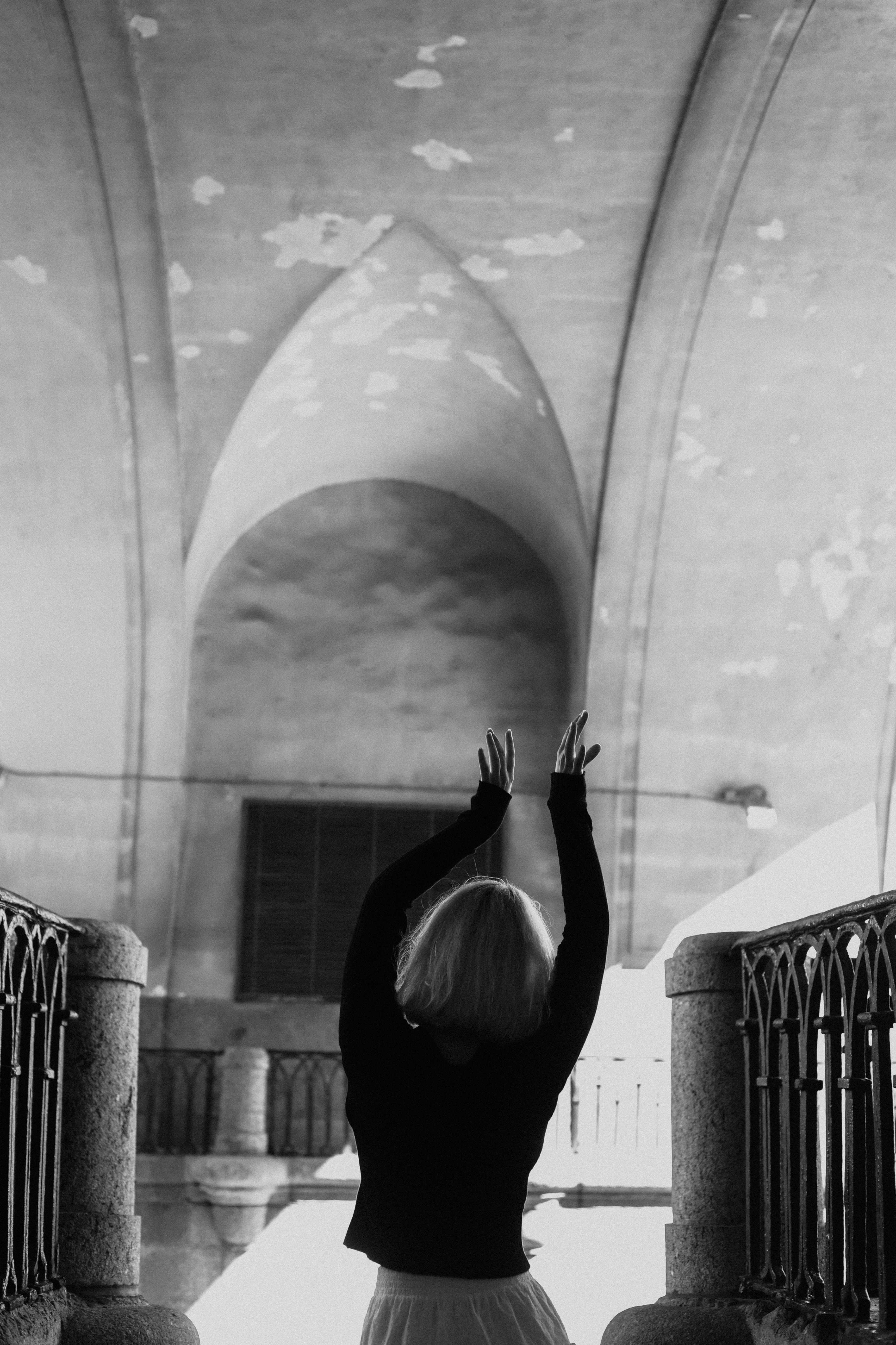 Black and white photo of a woman with raised arms under a grand arched interior.