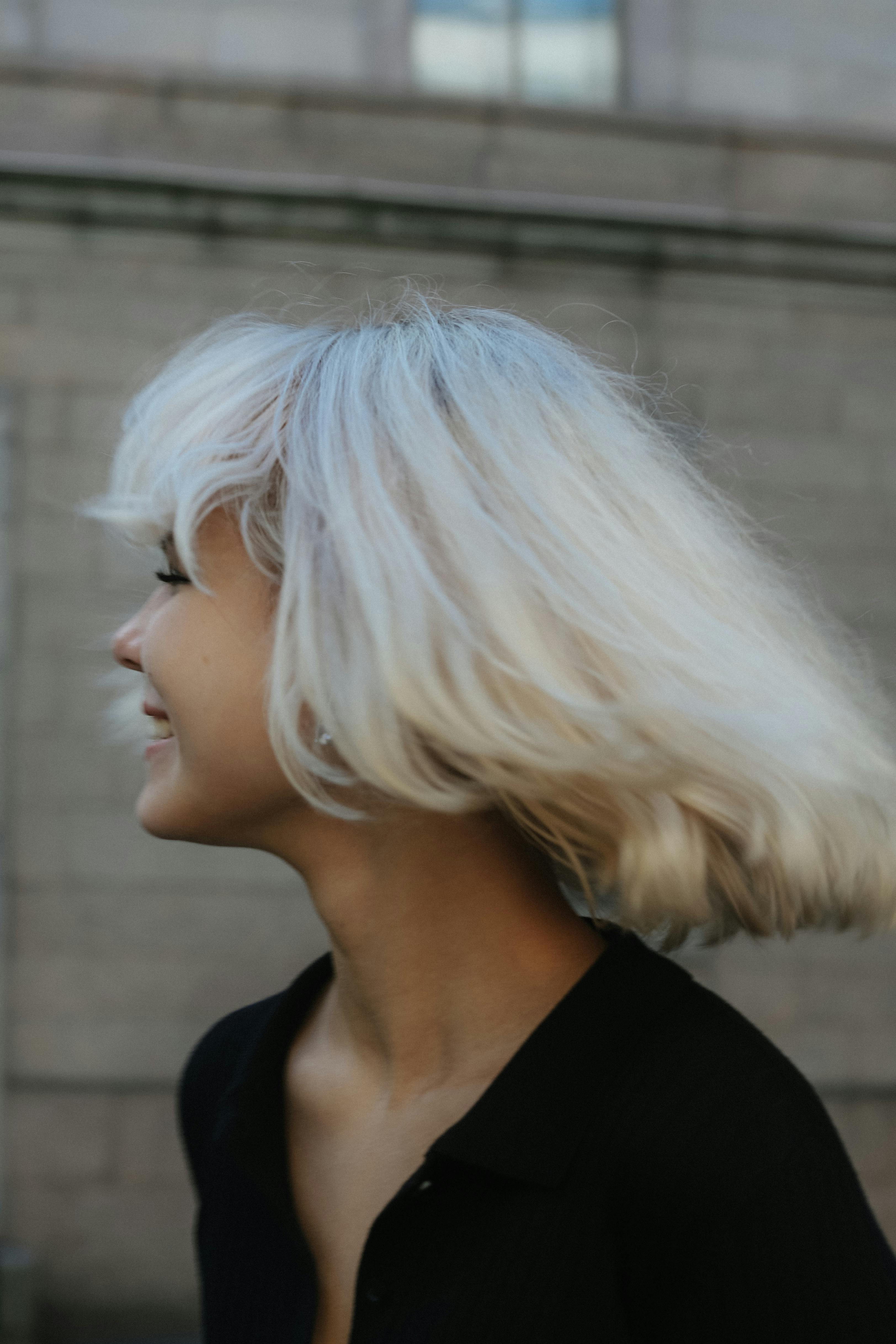 A woman with platinum blonde hair smiles outdoors, showcasing happiness and vibrant youth.
