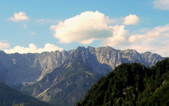Breathtaking view of the rocky Walchsee Alps with lush forests under a clear blue sky.