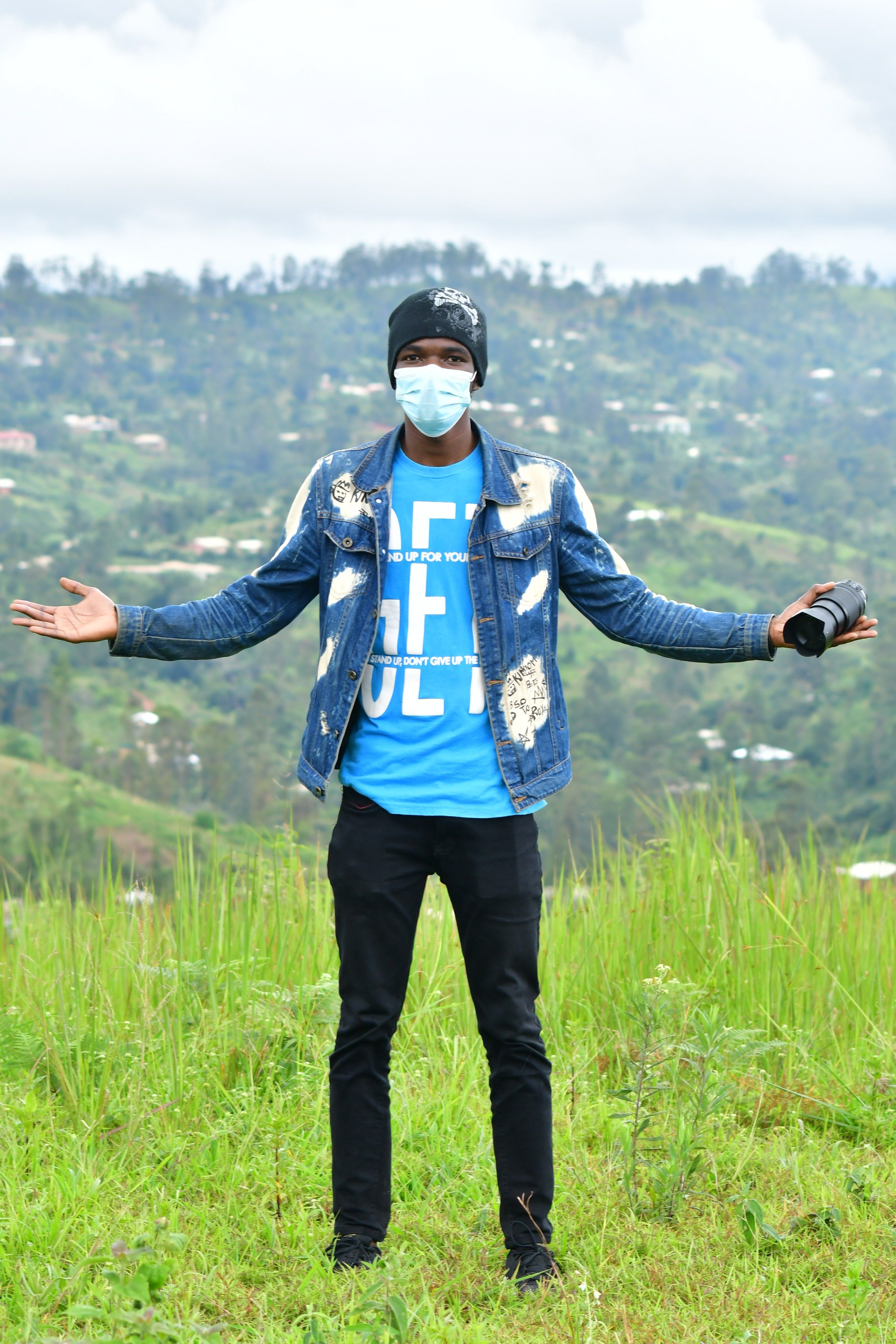 A man in a denim jacket stands on a hilltop with arms open, embracing the natural landscape.