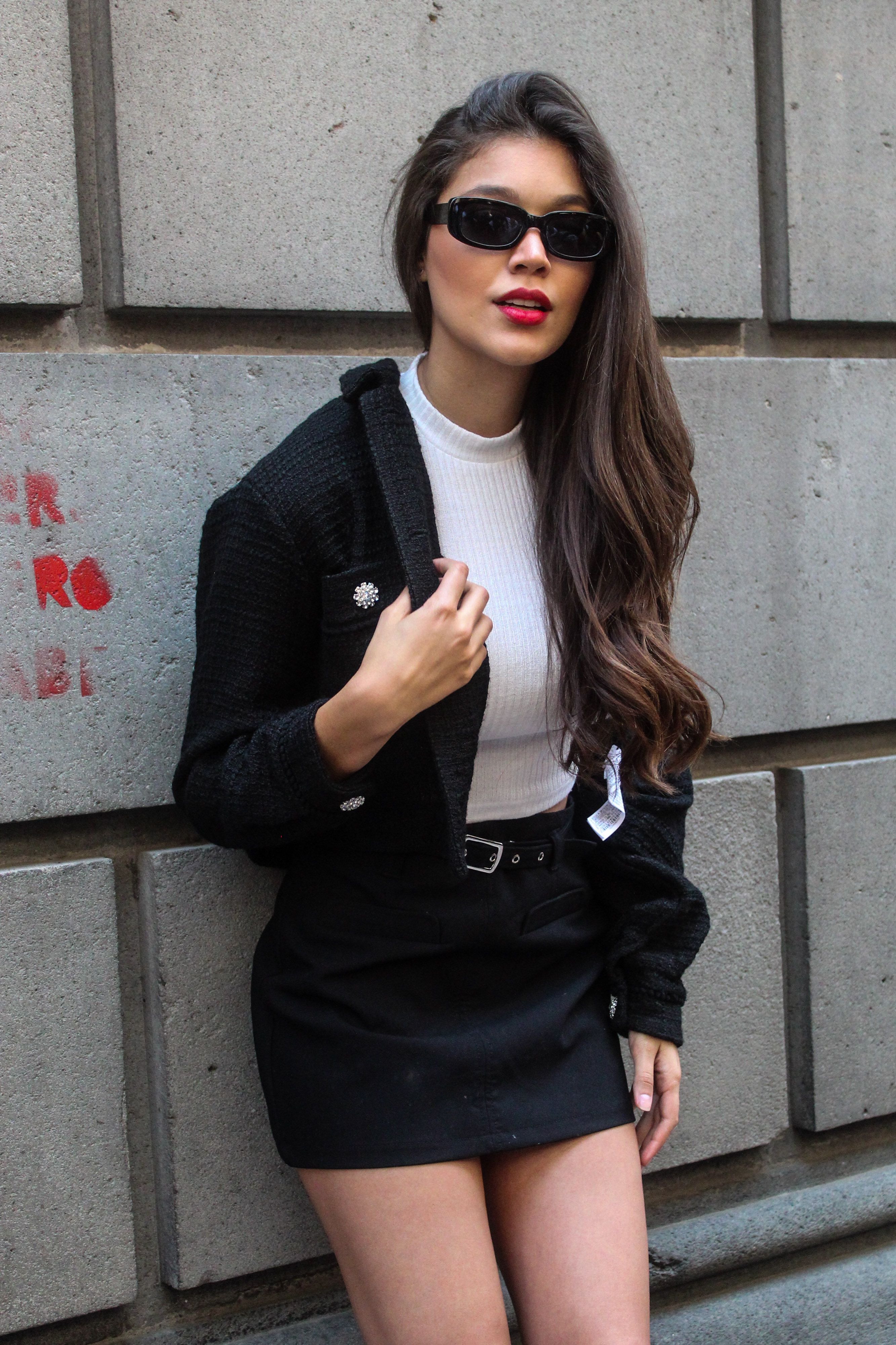 Stylish woman posing against a concrete wall in a black blazer and skirt.