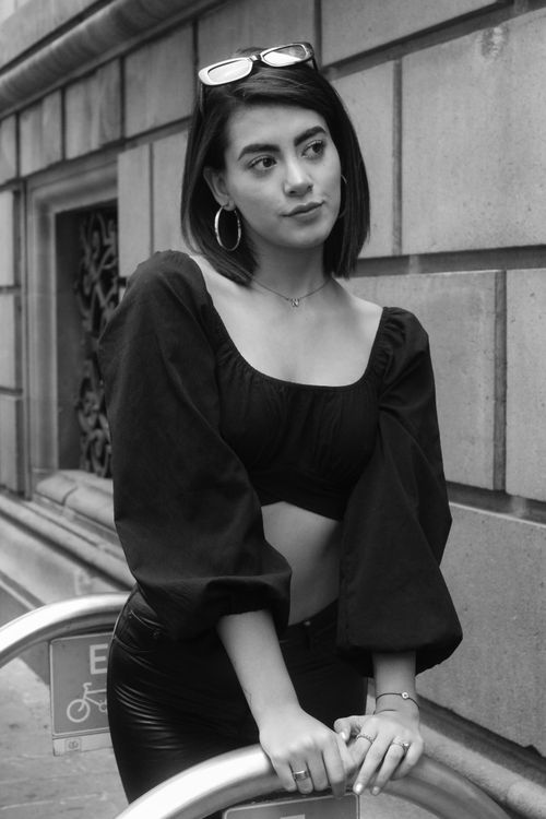 Free Black and white portrait of a woman in a trendy crop top posing against a city backdrop. Stock Photo
