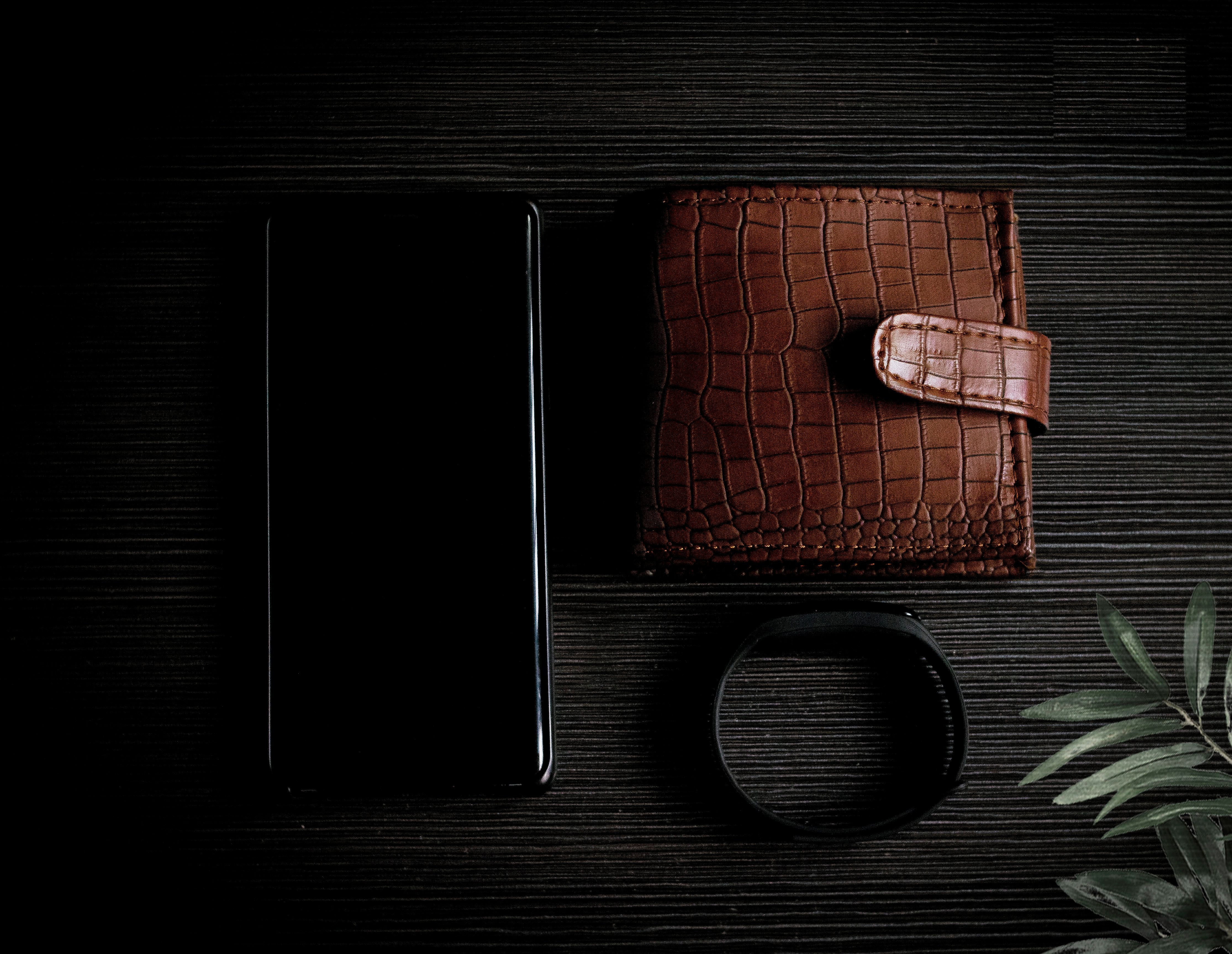 Elegant composition of a leather wallet, smartphone, and watch on a wooden surface.