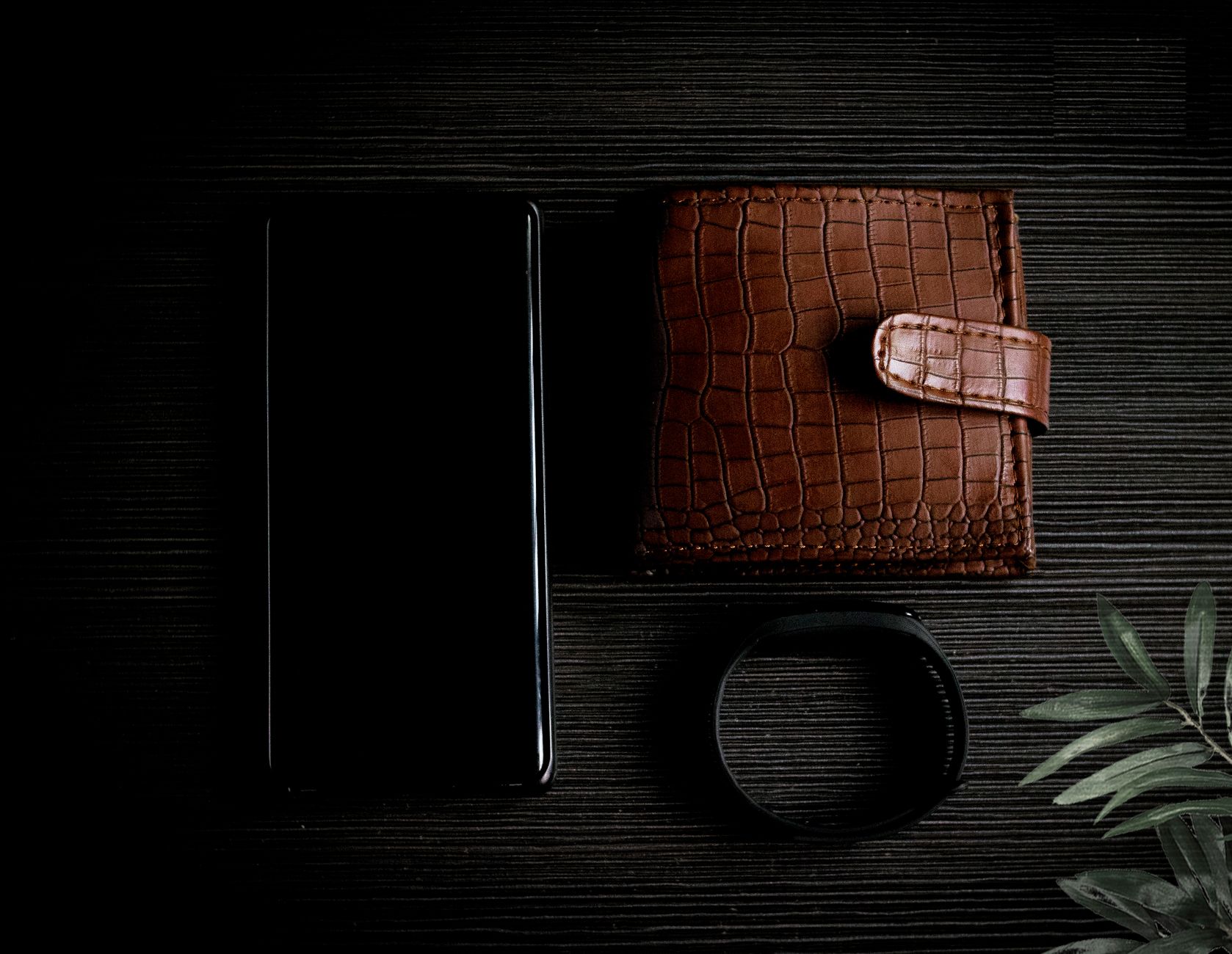 Elegant composition of a leather wallet, smartphone, and watch on a wooden surface.