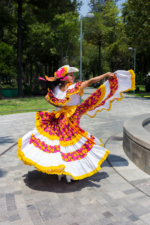 Free A woman in colorful traditional dress dancing gracefully in a sunlit park setting. Stock Photo
