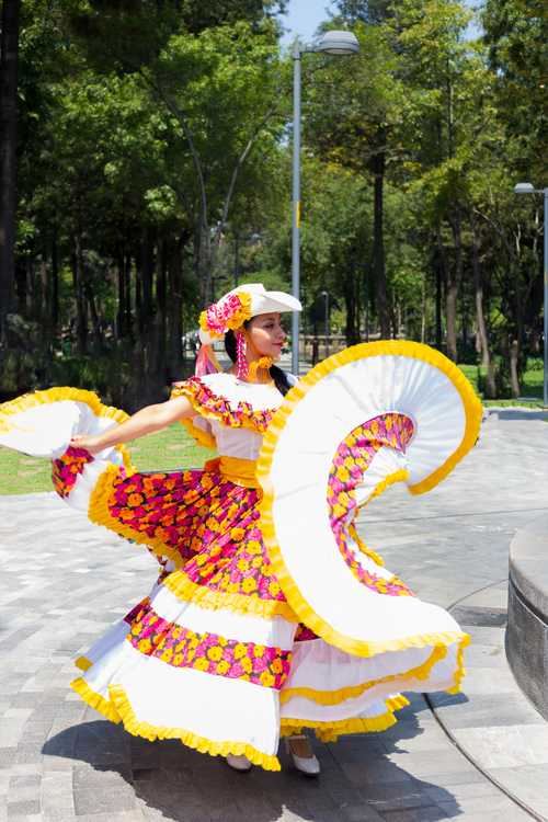 Free Woman performing a traditional Mexican dance in a vibrant, colorful dress in a sunny park setting. Stock Photo