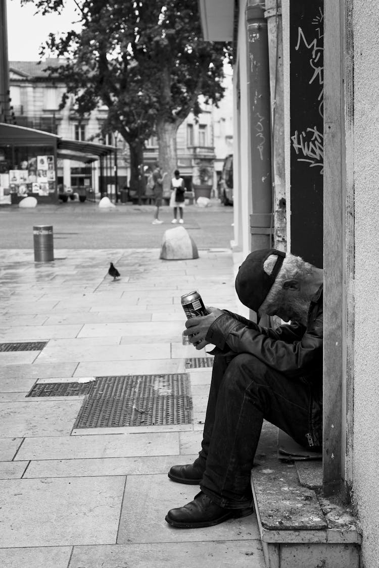 Grayscale Photo Of A Drunk Old Man Sleeping While Sitting On Doorway