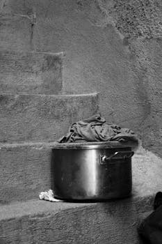 Black and white image of a rustic cooking pot on concrete stairs, conveying a vintage feel.