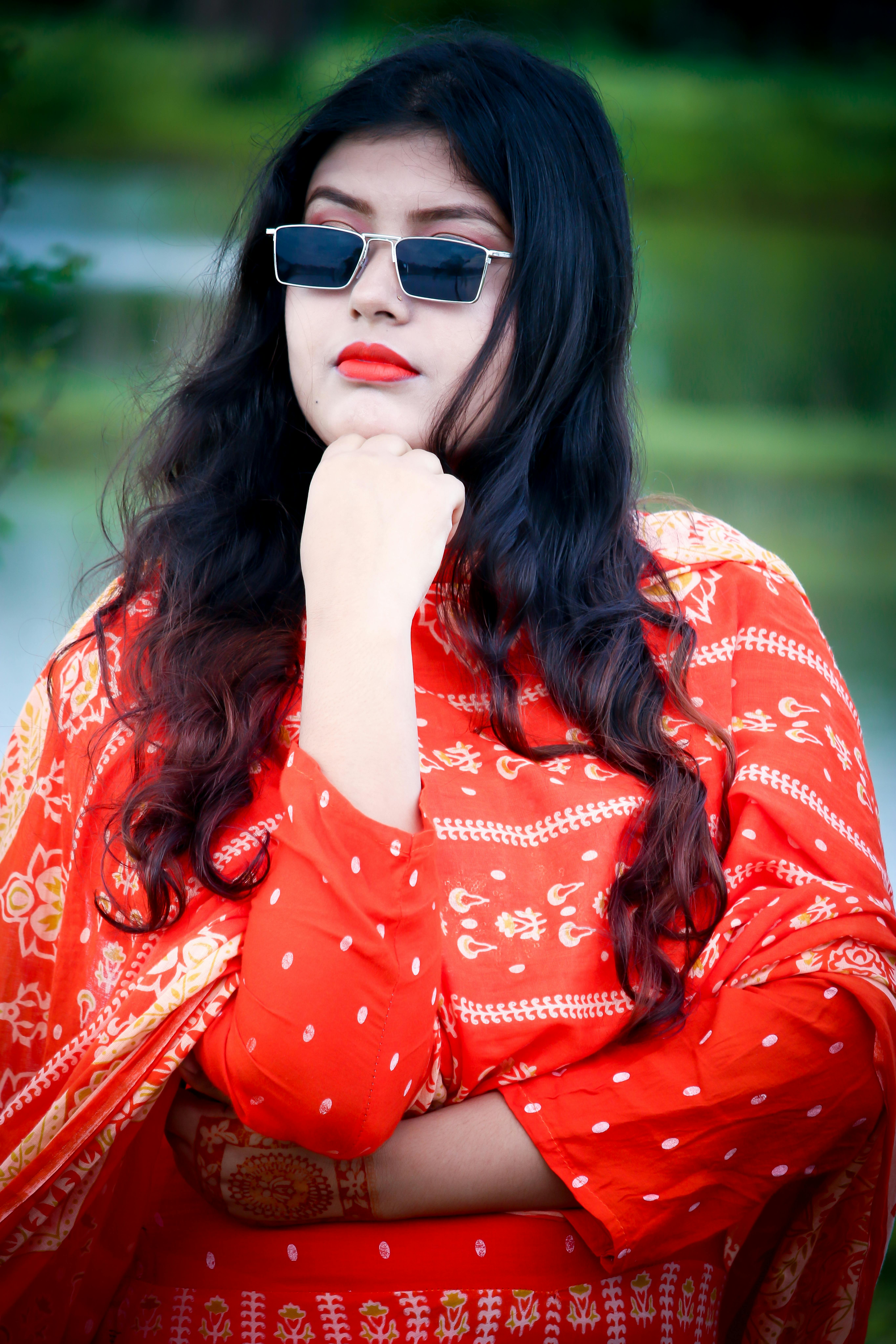 Confident woman wearing red saree and sunglasses in an outdoor setting.