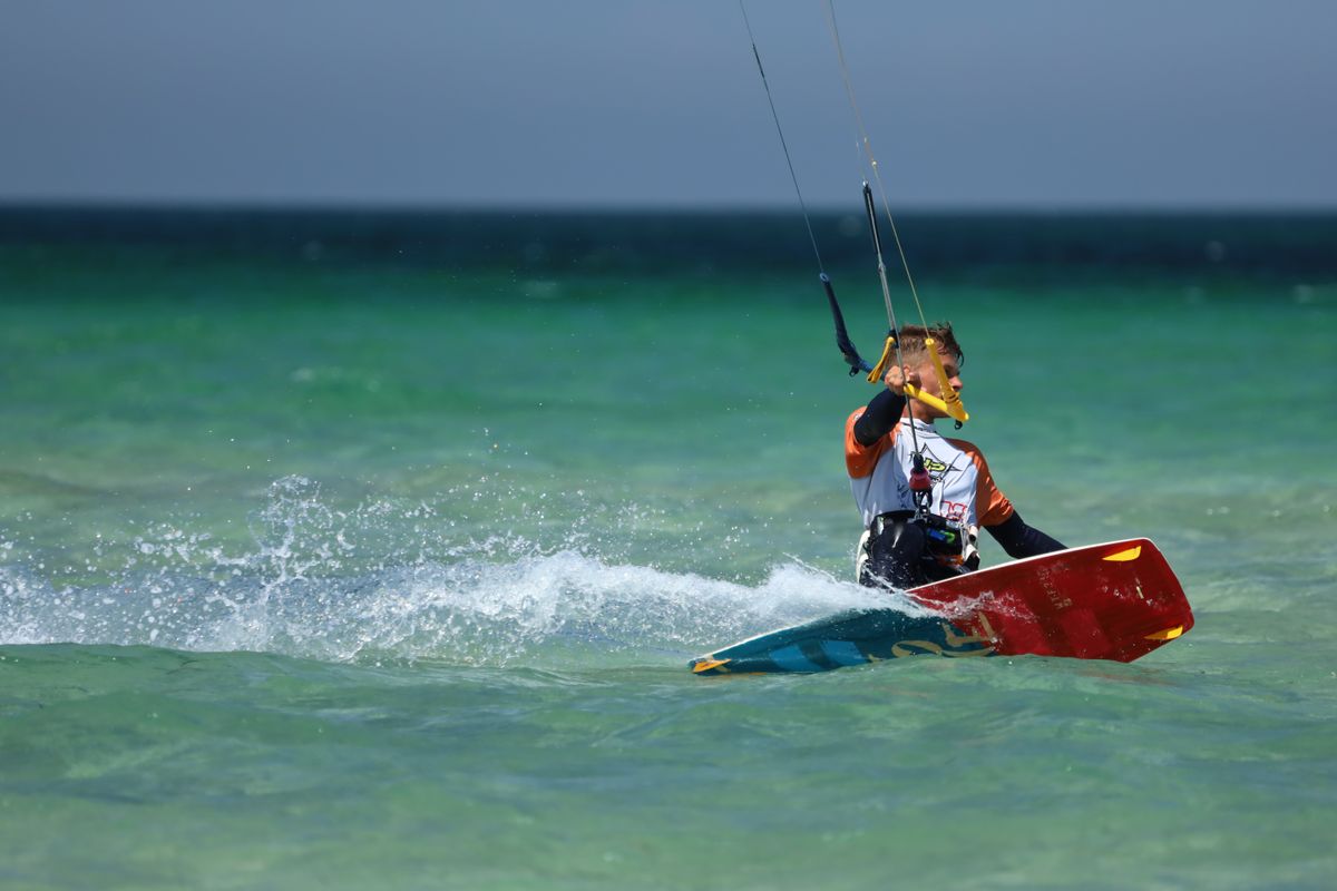 Kitesurfer riding waves over turquoise ocean water on a sunny day