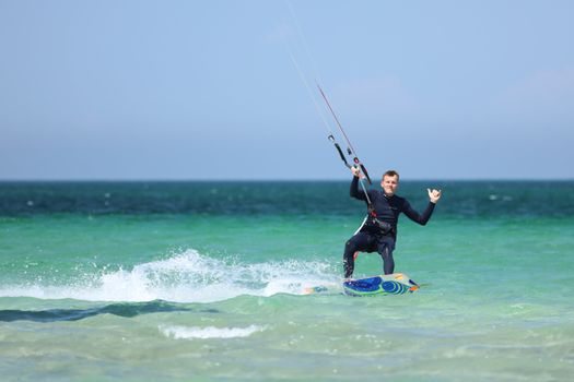 A man enjoys kiteboarding on a sunny day with clear blue waters and bright sky.