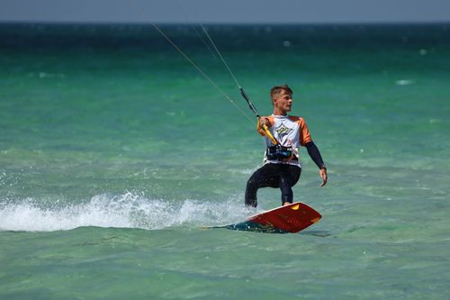 Free A dynamic shot of a man kiteboarding on turquoise waters, showcasing the thrill of the sport. Stock Photo