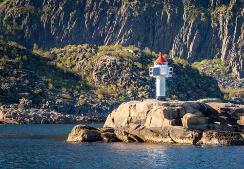 Free A lighthouse stands on a rocky shore surrounded by dramatic cliffs in Norway. Stock Photo