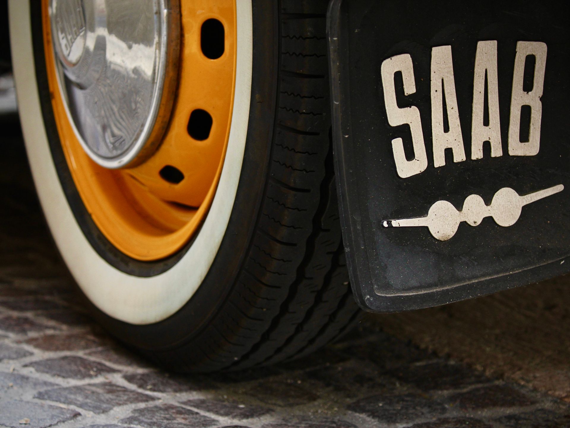 Close-up of a vintage Saab car wheel highlighting orange rim and branded mud guard.