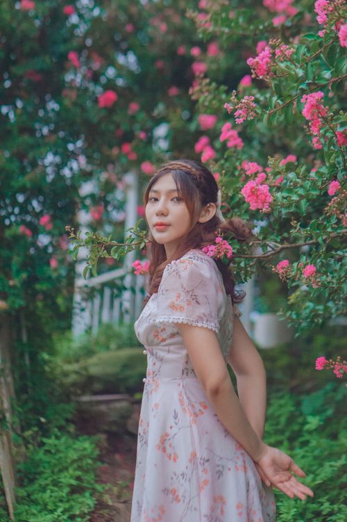 Free A young woman in a pink floral dress poses gracefully in a lush, vibrant garden. Stock Photo
