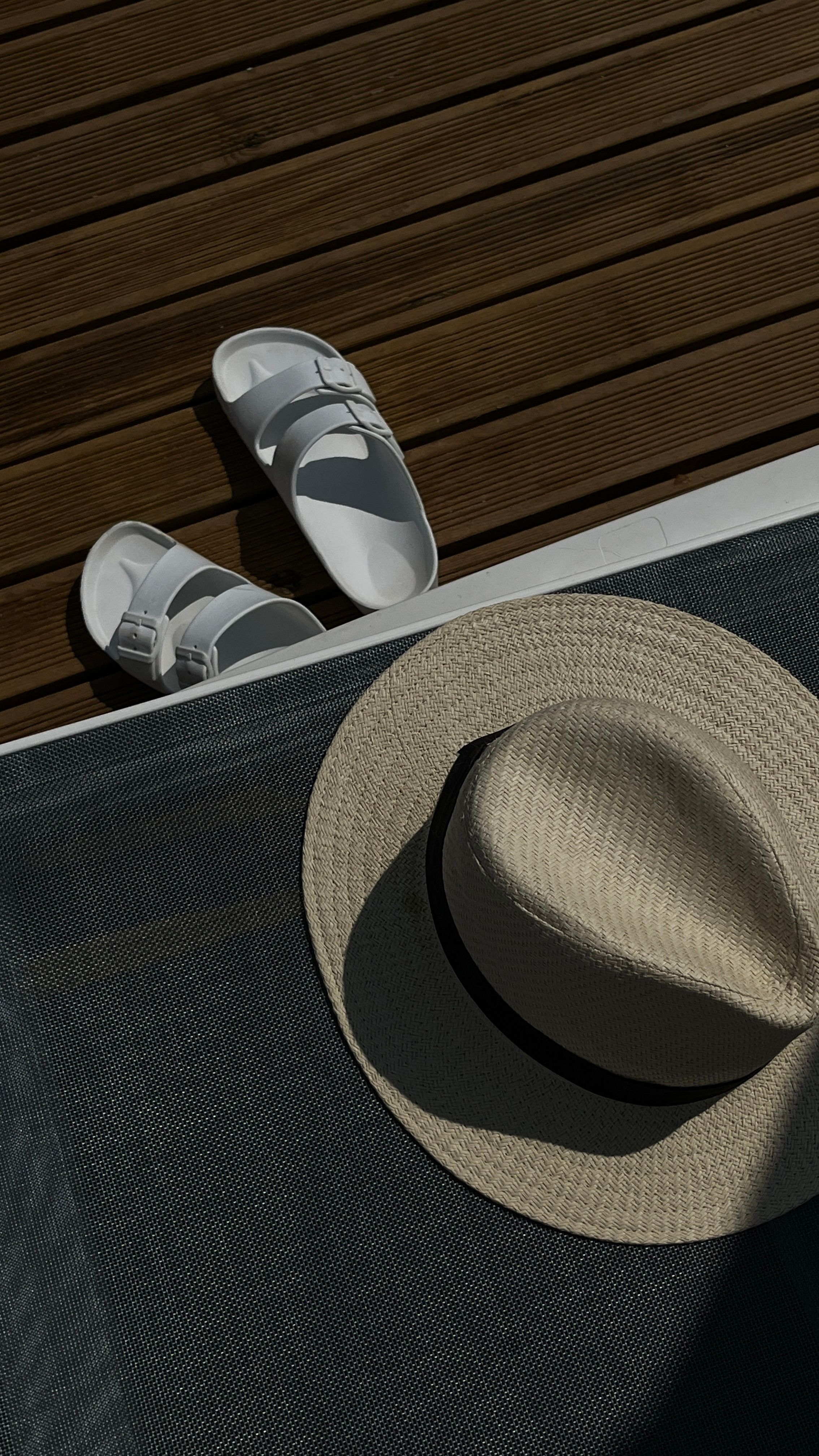 Straw hat and white sandals on a wooden deck in Assos, Turkey.