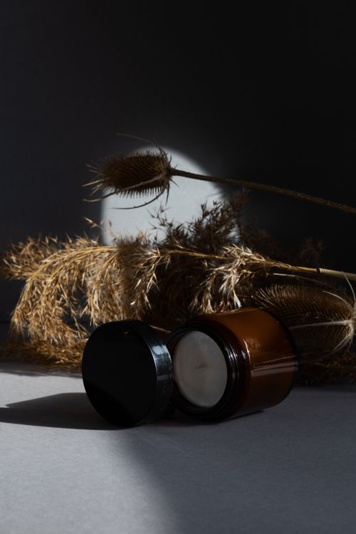 Free Brown glass jar with cream next to dried grasses in artistic light. Stock Photo
