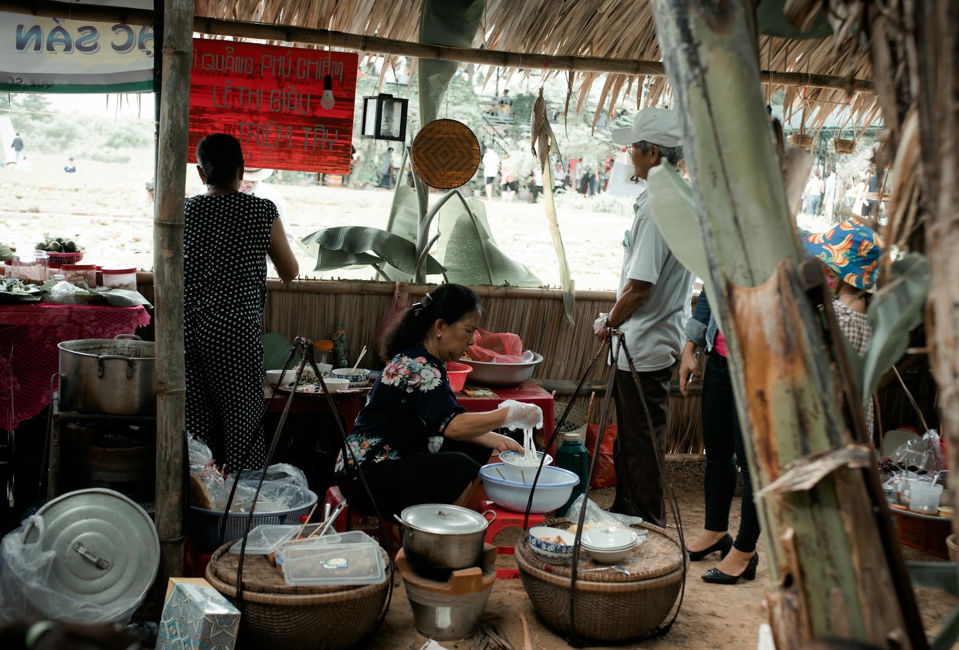 Authentic scene of people preparing food at a traditional market stall under a thatched roof.