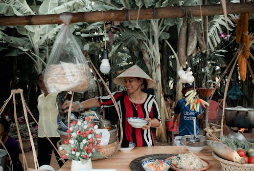 Asian woman vendor serving food in a vibrant outdoor market with tropical surroundings.