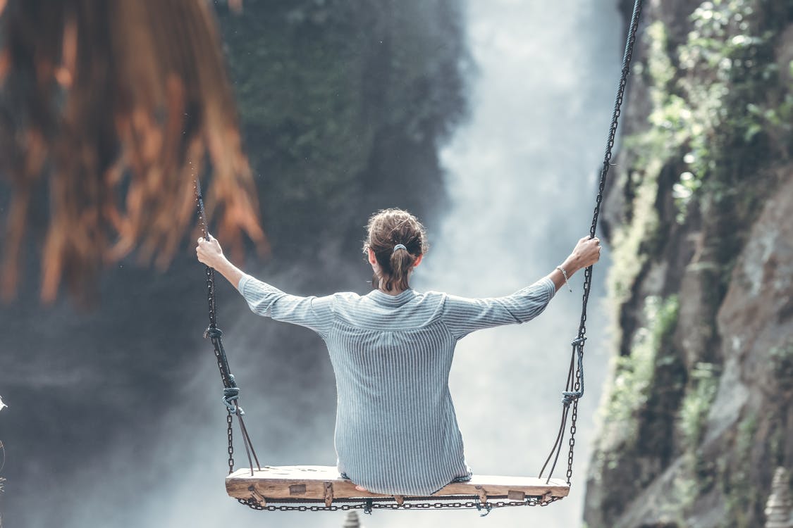 Woman Riding Big Swing in Front of Waterfalls