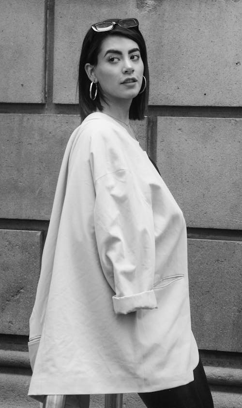 Grayscale Photo of Woman in White Blazer Standing Near Concrete Wall