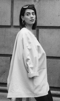 Grayscale side view of a woman wearing an oversized blazer and hoop earrings.